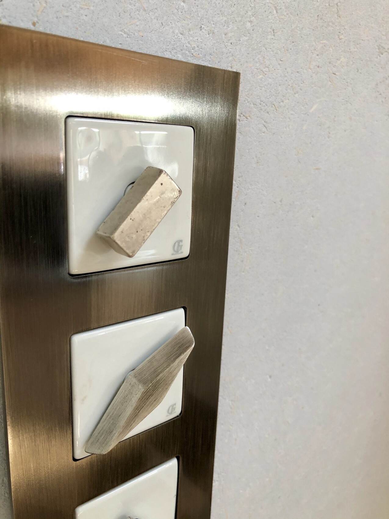 Drei weiße, quadratische Lichtschalter in einer brünierten Metallrahmen-Wandplatte.