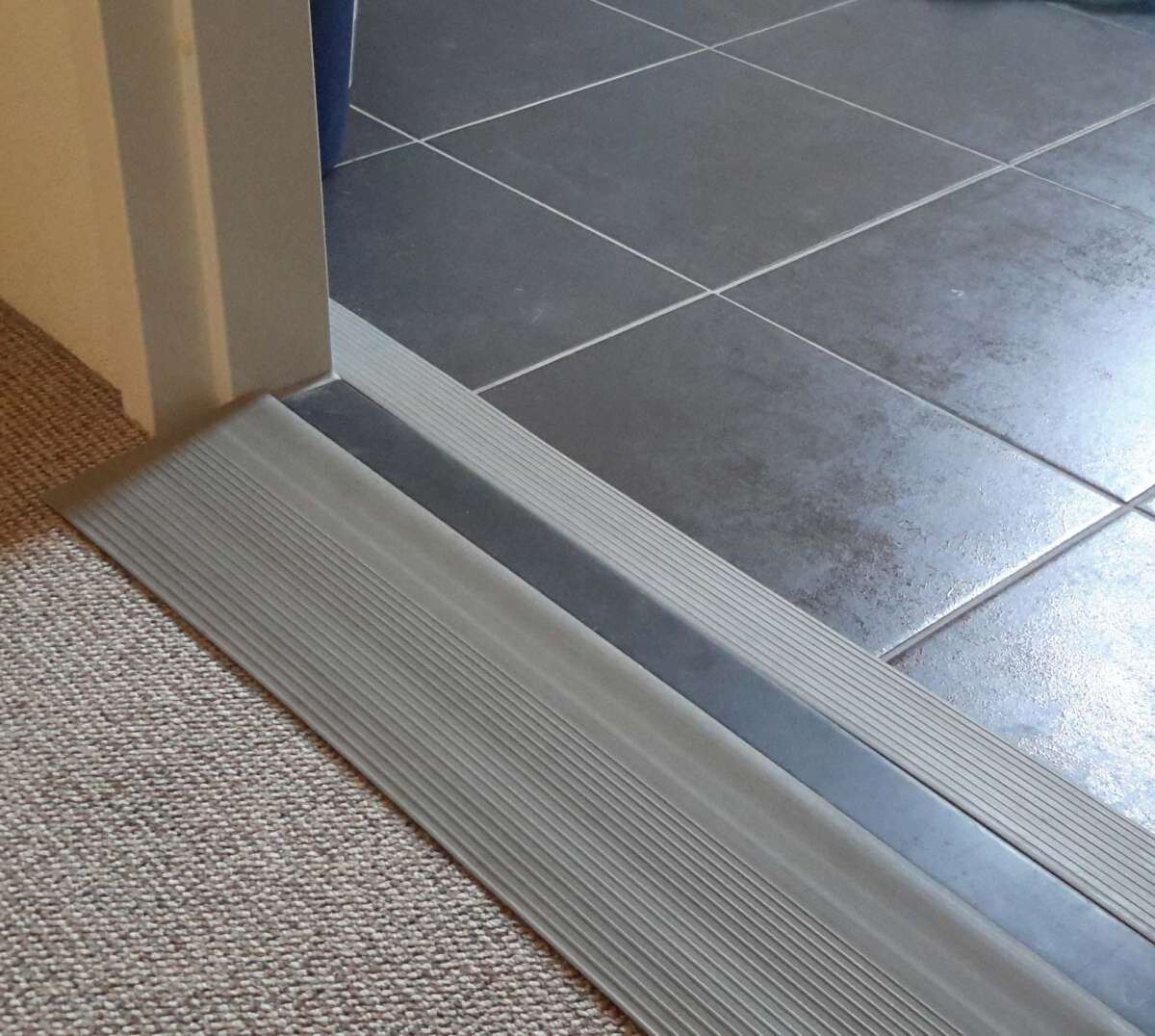 Türschwelle aus Metall mit geriffelter Oberfläche zwischen Teppichboden und Fliesen.