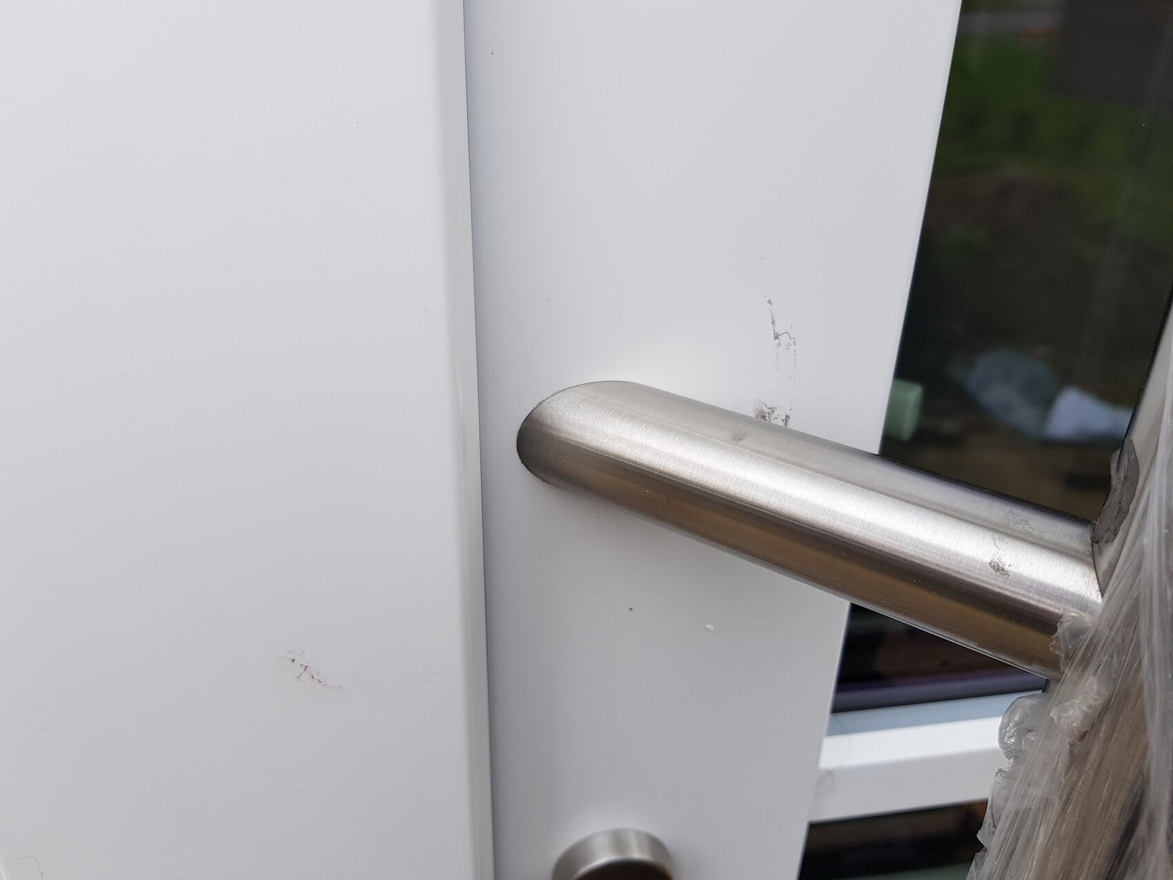 Nahaufnahme eines Edelstahl-Türgriffs an einer weißen Tür mit Fenster