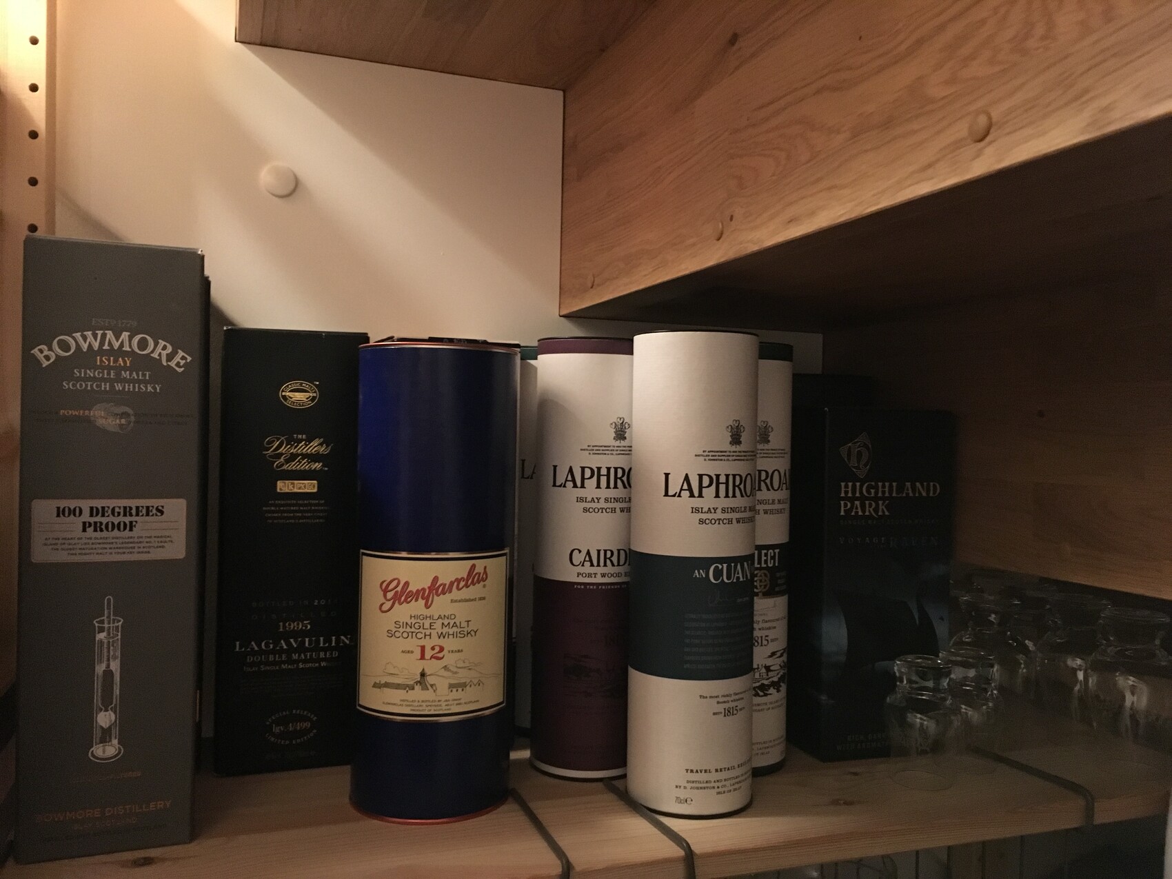 Holzregal mit Whisky-Kisten und Flaschen, Marken Bowmore, Lagavulin, Glenfarclas, Laphroaig.