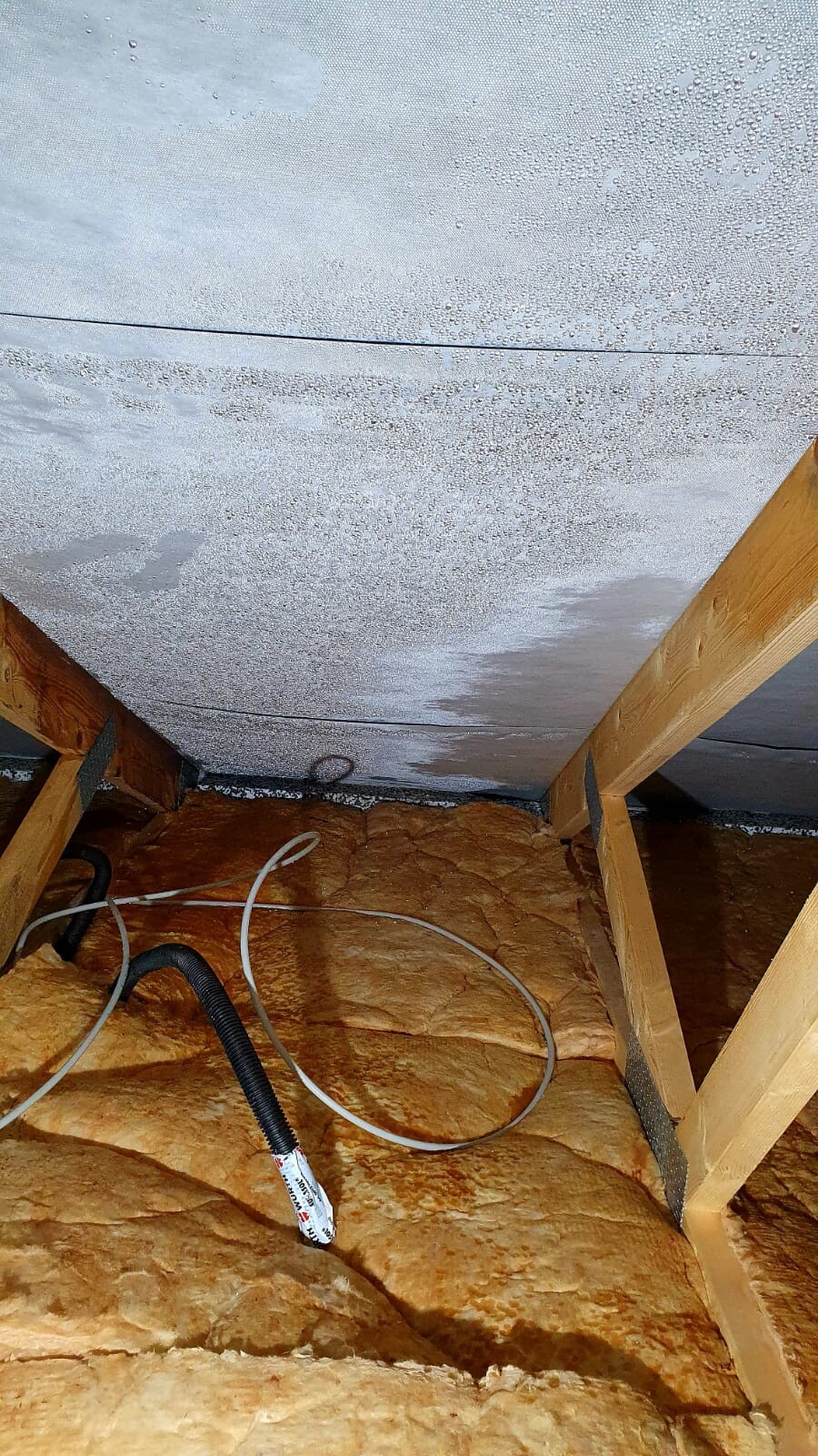 Dachboden mit Holzstützen, gelber Dämmstoff, silberner Deckenisolierung und Kabel.