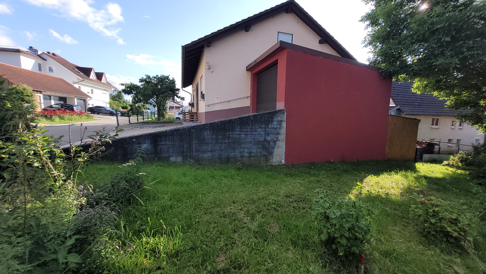 Außenansicht eines Einfamilienhauses mit roter Anbauwand und Garten