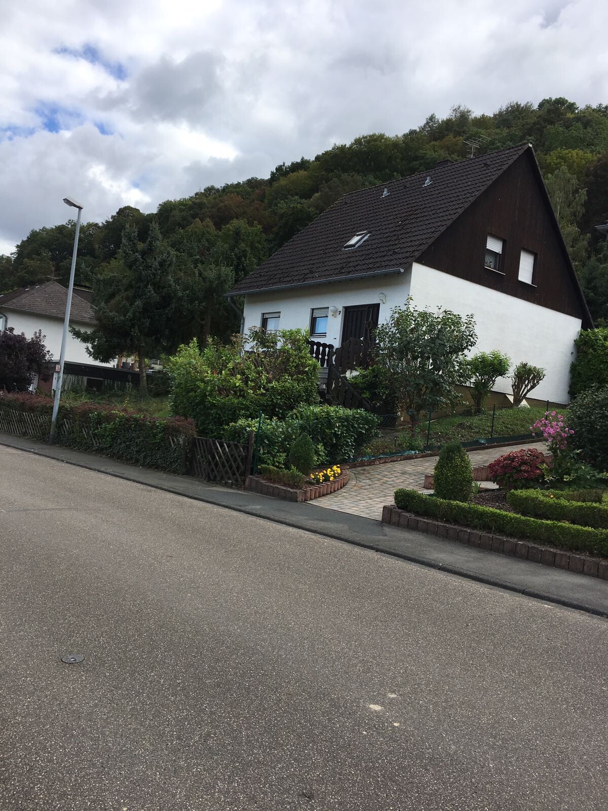 Einfamilienhaus mit weißer Fassade, dunklem Dach, Garten und gepflastertem Vorplatz an der Straße