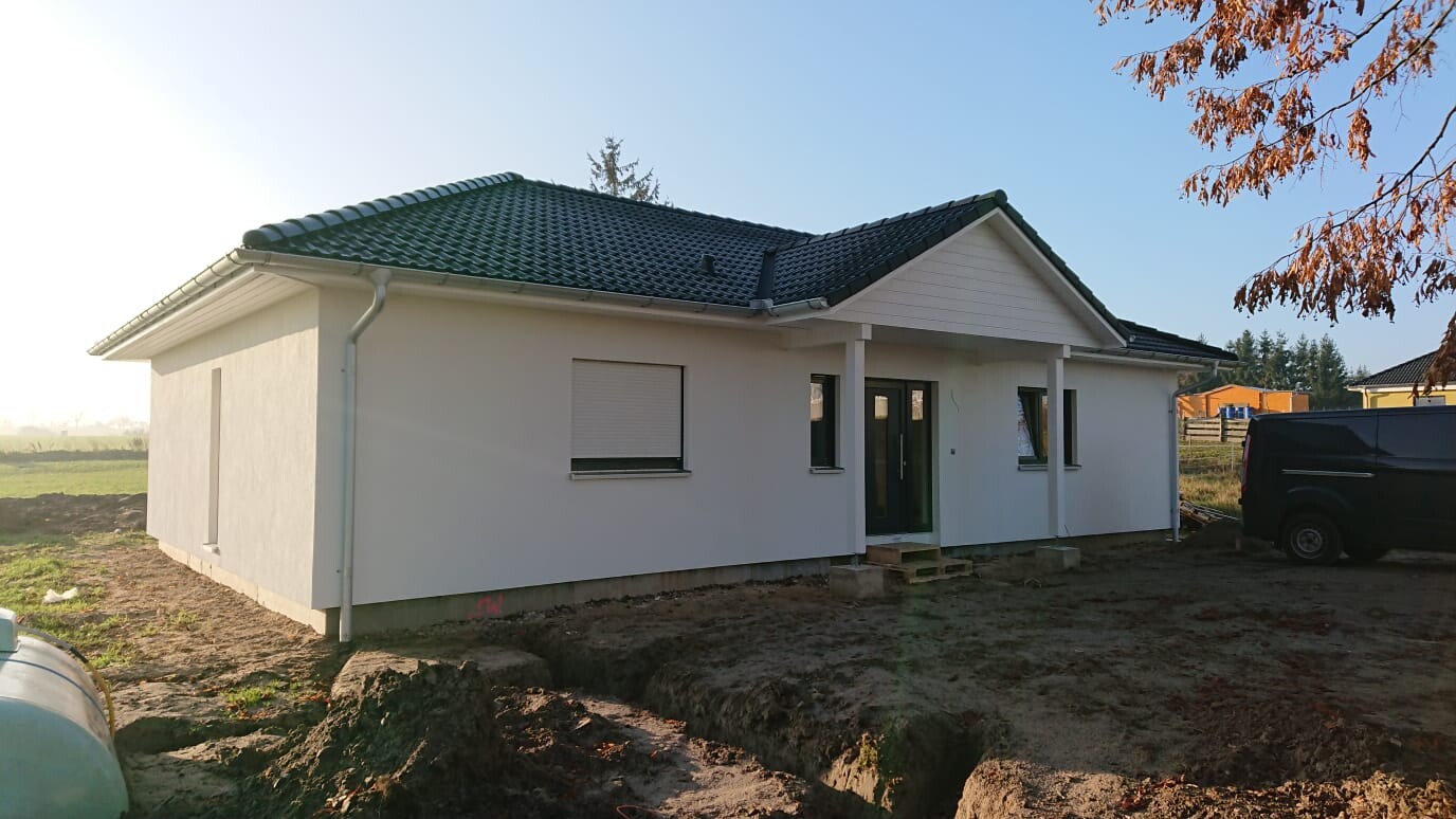 Weiße Einfamilienhaus-Baustelle mit dunklem Ziegeldach, Vordach, Fenstern und schwarzem Van.