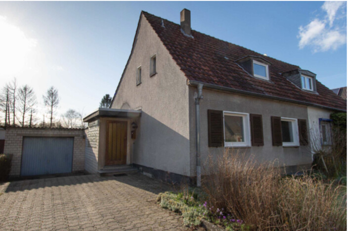 Zweistöckiges Haus mit rotem Satteldach, Fensterläden, Eingangsvorbau und Garage links
