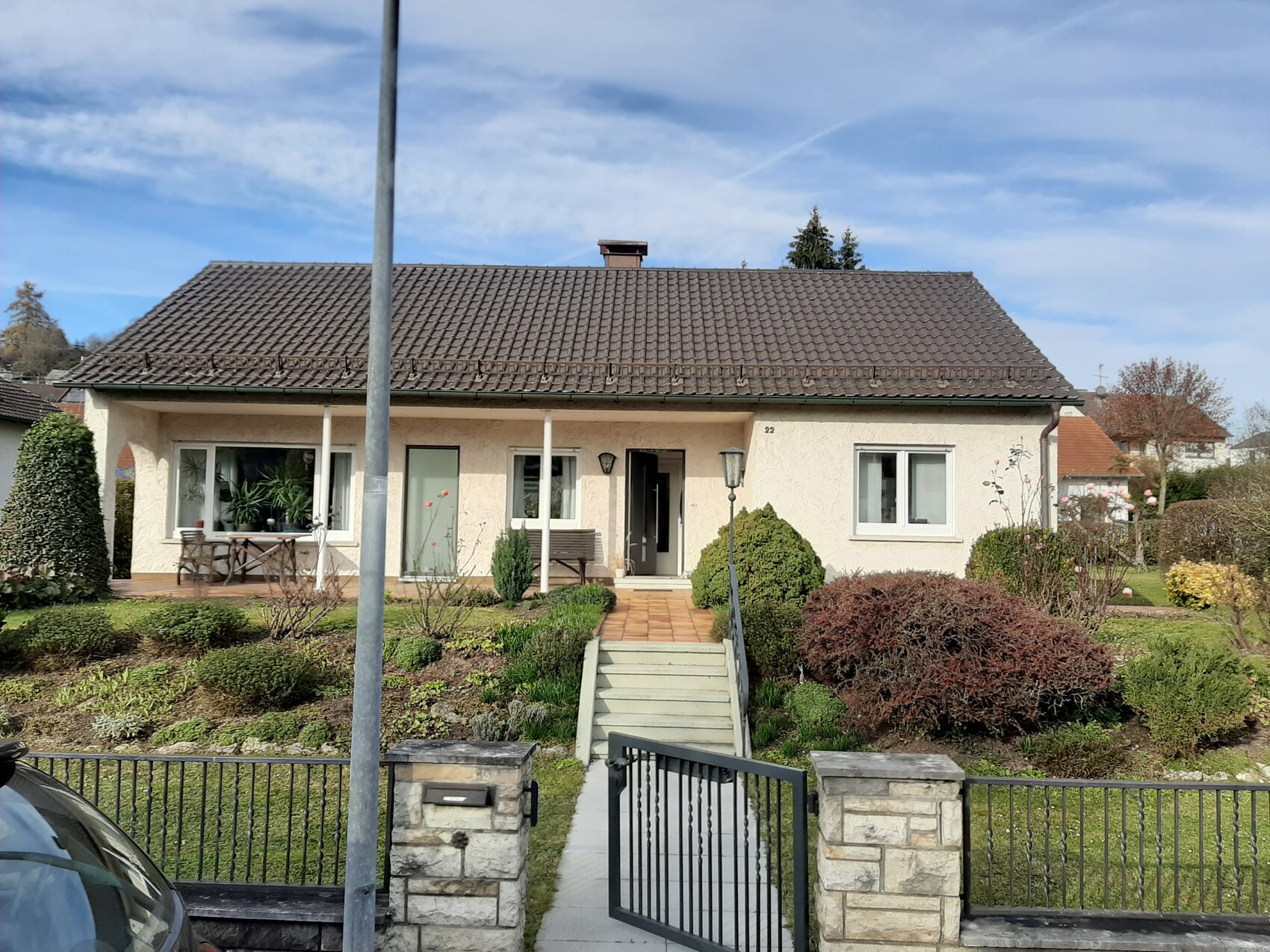 Einfamilienhaus mit braunem Dach, beige Fassade, Treppenweg zur Haustür, Vorgarten und Zaun.