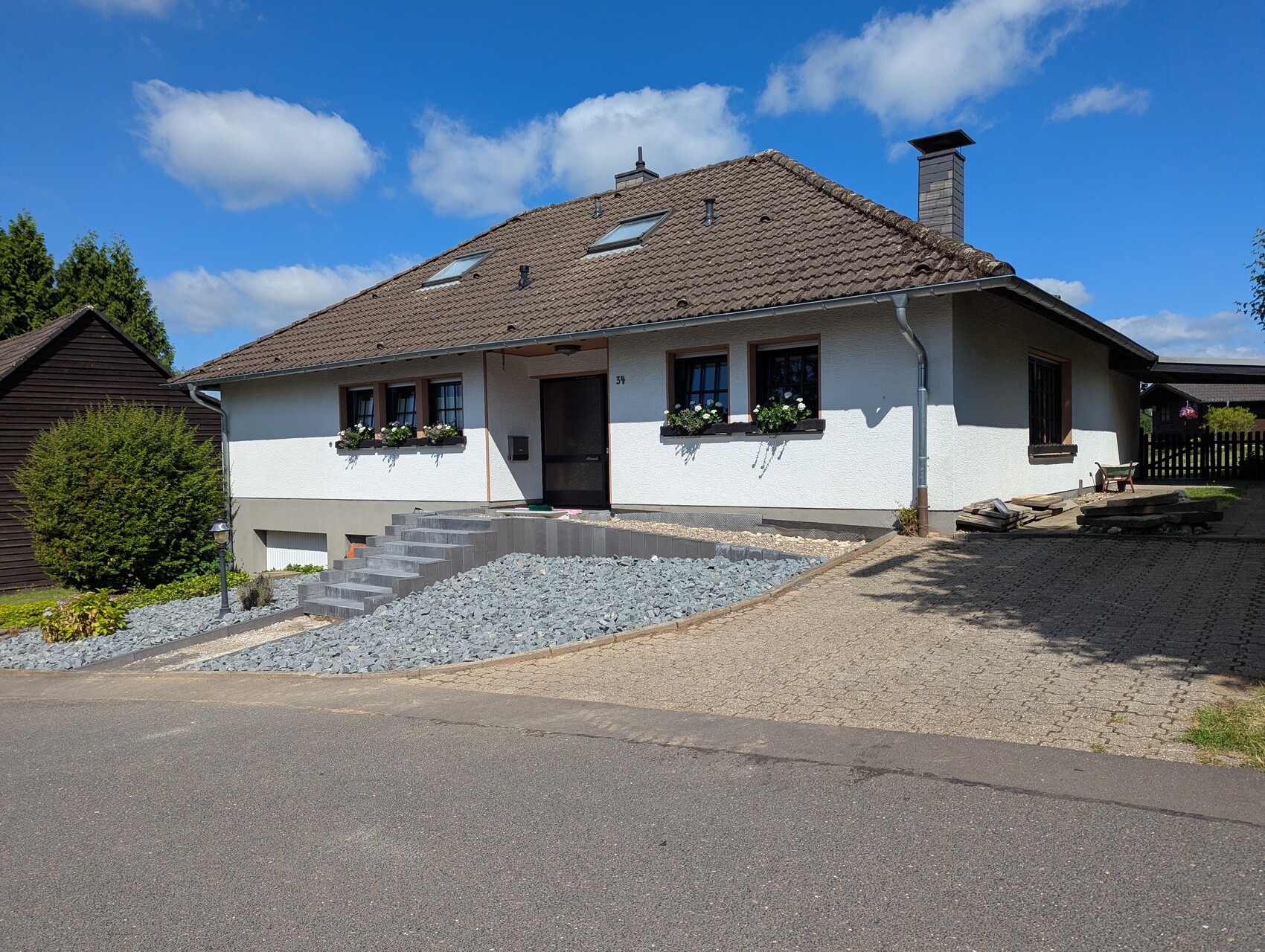 Weißes Einfamilienhaus mit braunem Dach, Treppe zum Eingang und Blumenkästen unter den Fenstern.