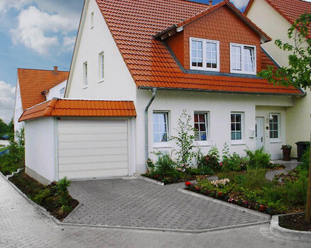 Außenansicht eines weißen Einfamilienhauses mit rotem Dach und Garage an der Zufahrt.