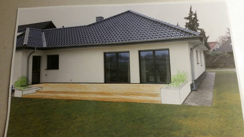 Außenansicht eines Einfamilienhauses mit Holzterrasse, großen Glasfenstern und Gartenfläche.