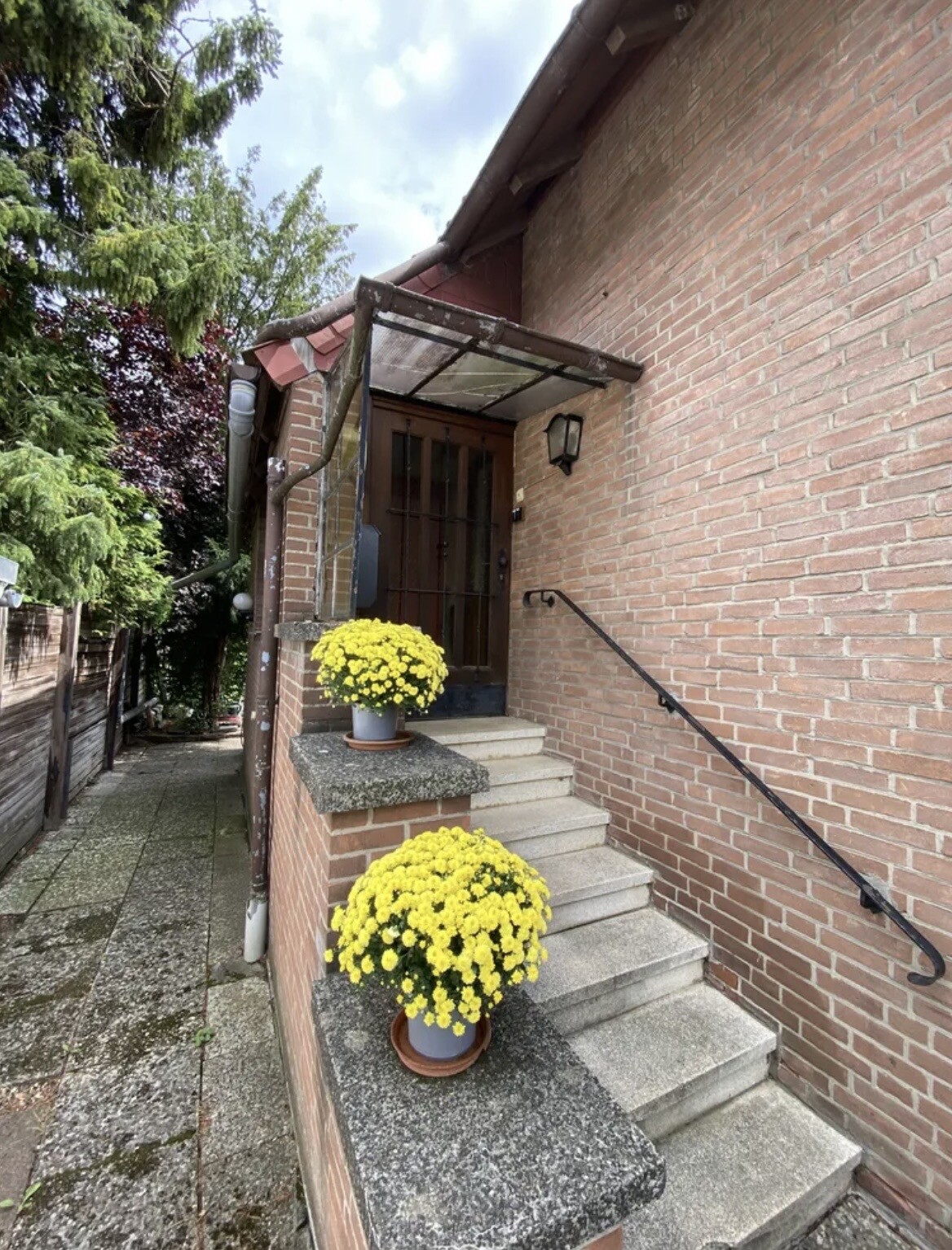 Fronteingang eines Backsteinhauses mit Treppe, Gelb-Chrysanthemen in Töpfen und Vordach.