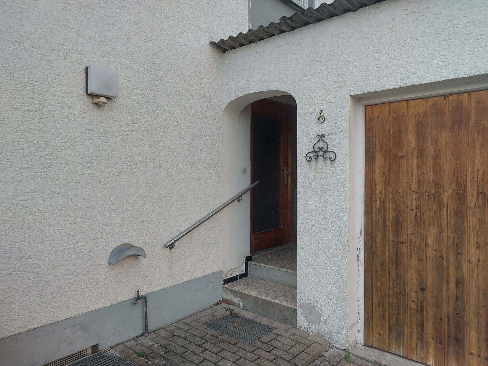 Außenansicht eines Eingangsbereichs mit gewölbtem Türbogen, Holztuer und Garagentor