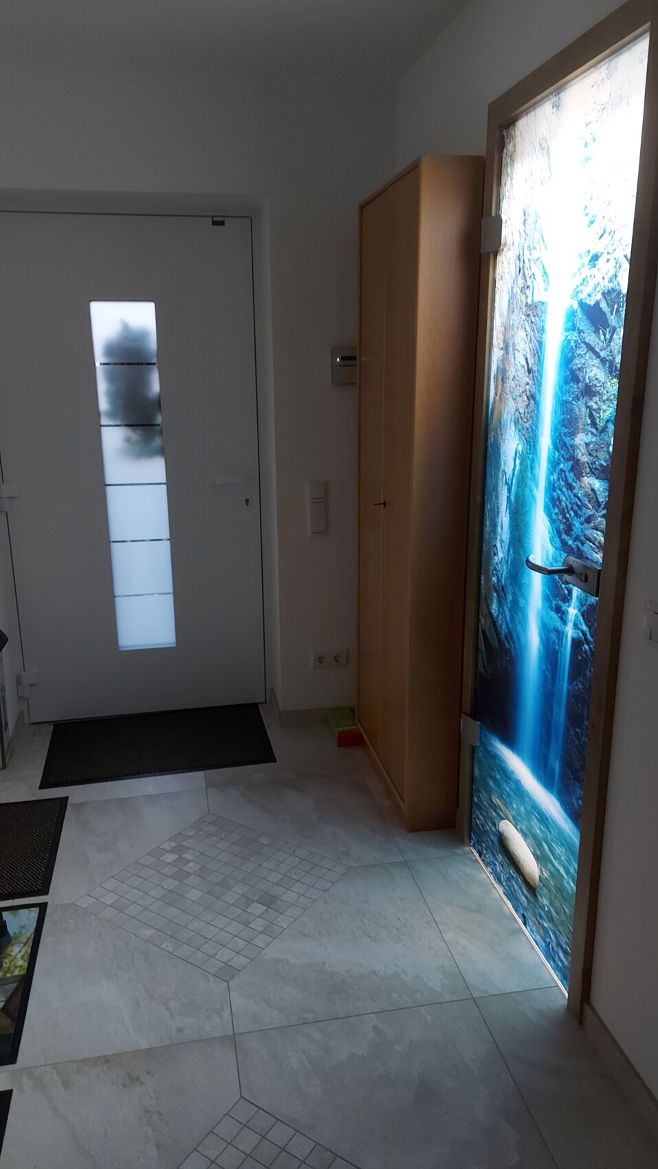 Eingang: weiße Tür mit Glasfenstern, Holzschrank, Tür mit Wasserfall-Bild.
