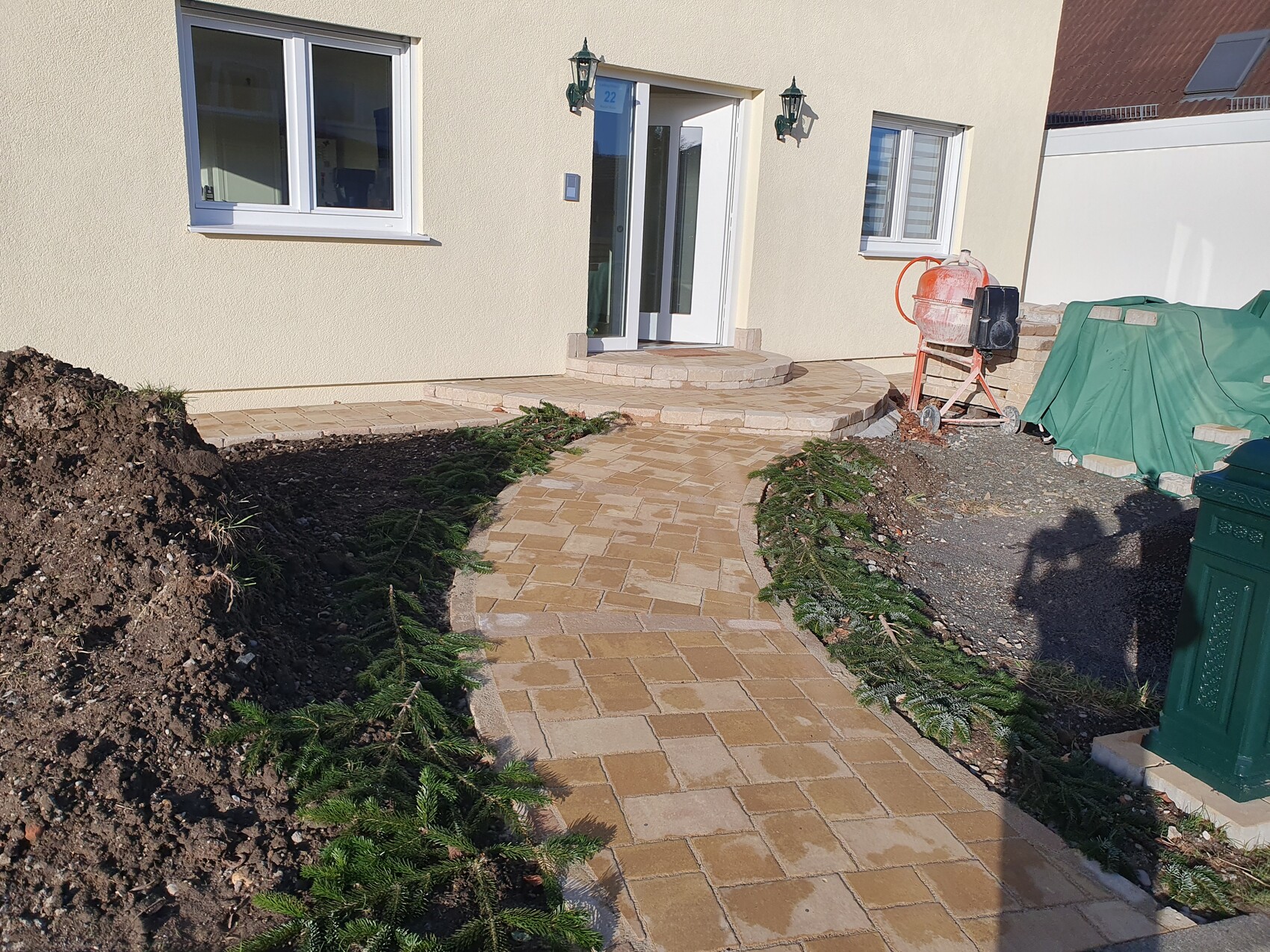 Vorderansicht eines hellen Hauses mit gepflastertem Weg zur Eingangstür; Bauausrüstung rechts.