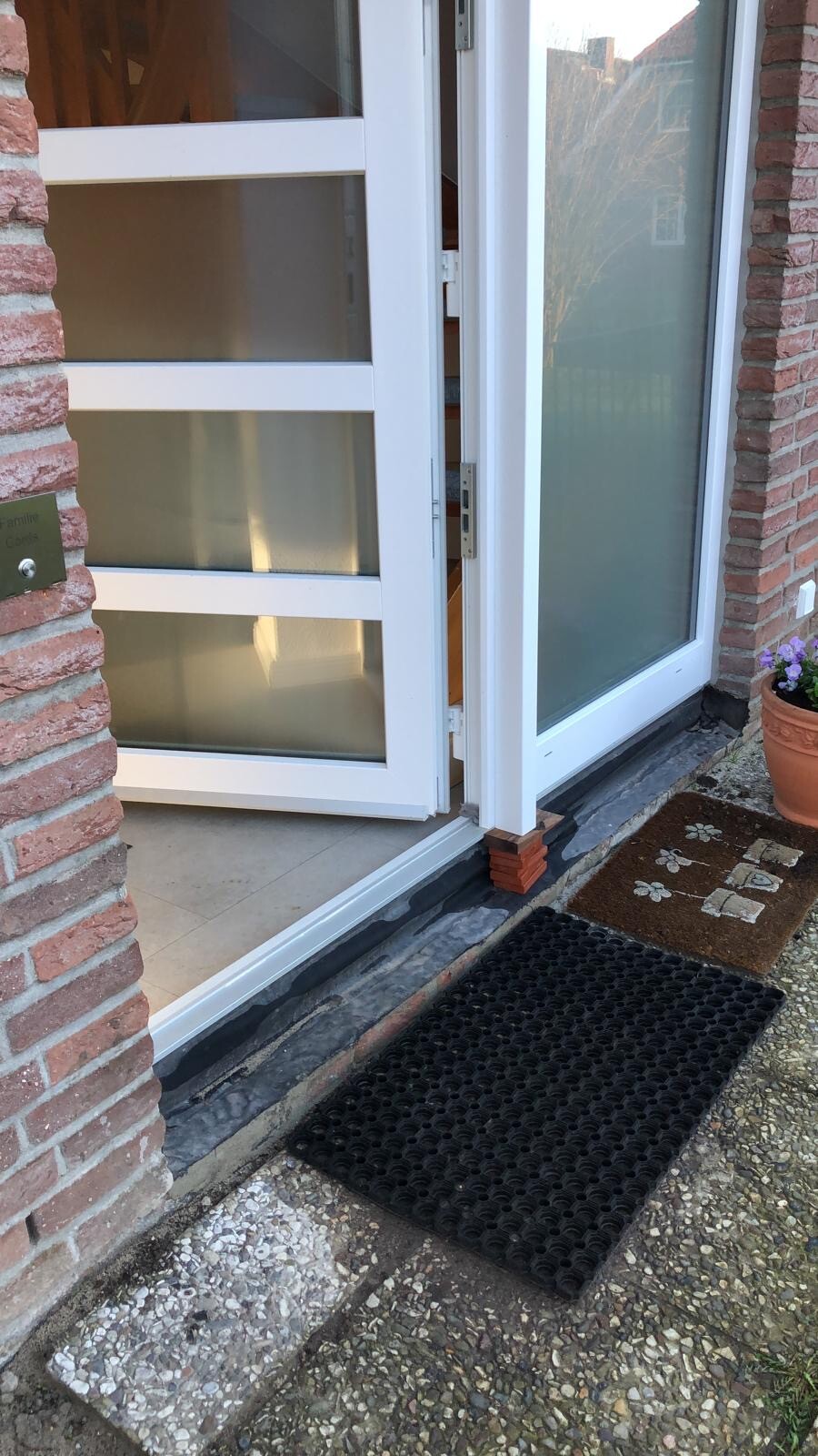 Weißer Eingang mit Glas-Tür vor roter Ziegelwand, schwarze Türmatte davor