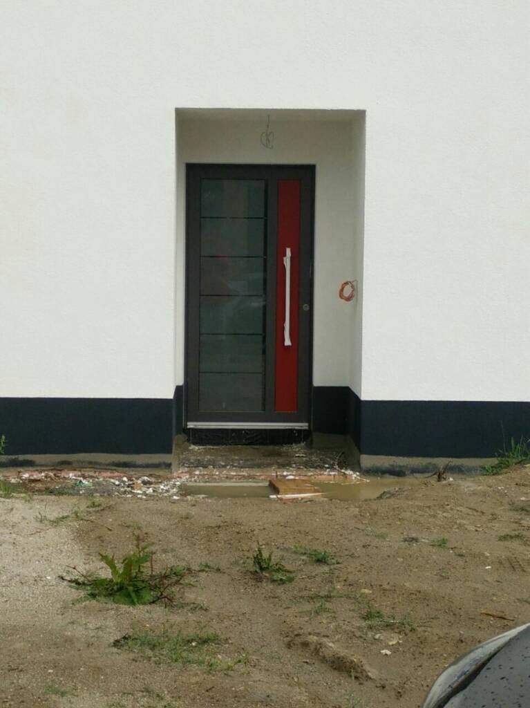 Fronttür eines Neubauhauses mit dunkler Glastür und rotem Streifen, Baustellenumgebung
