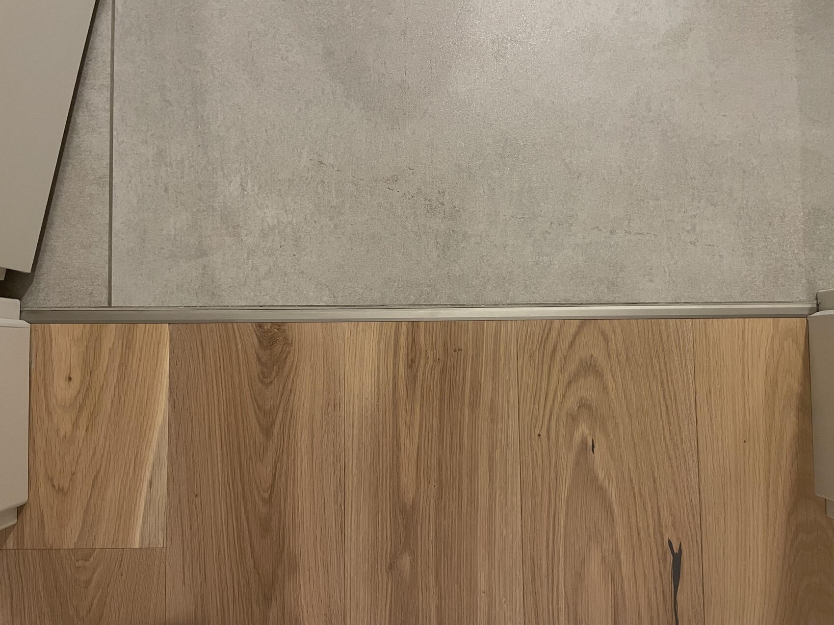 Türschwelle mit Metallprofil trennt grauen Bodenbelag oben vom Holzboden unten.
