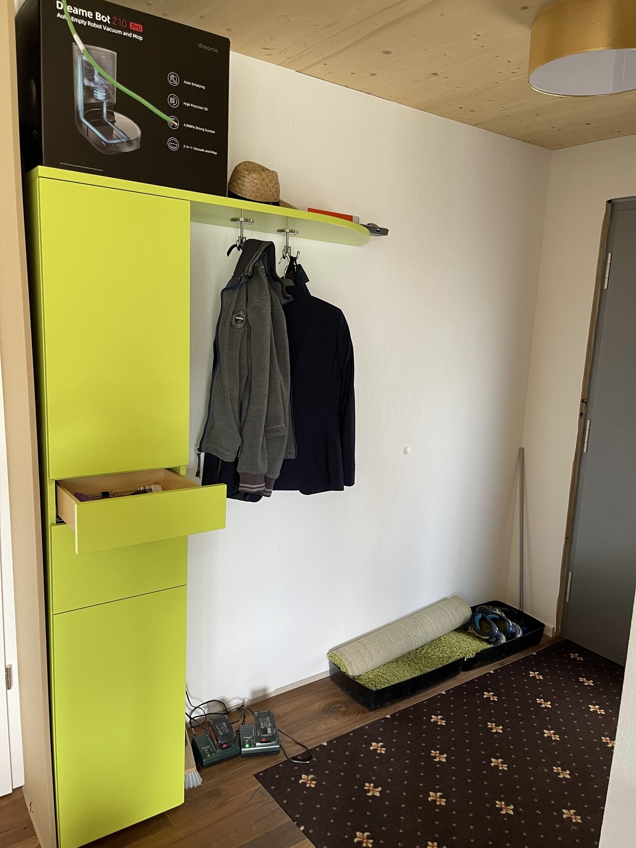 Flur mit neon-gruenem Kleiderschrank, Manteln, Haken, Schuhmatte und Tür.