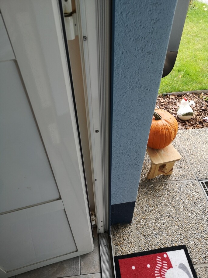 Offene Tür ins Freie; Kürbis auf kleinem Holzhocker neben einer Hühner-Deko.