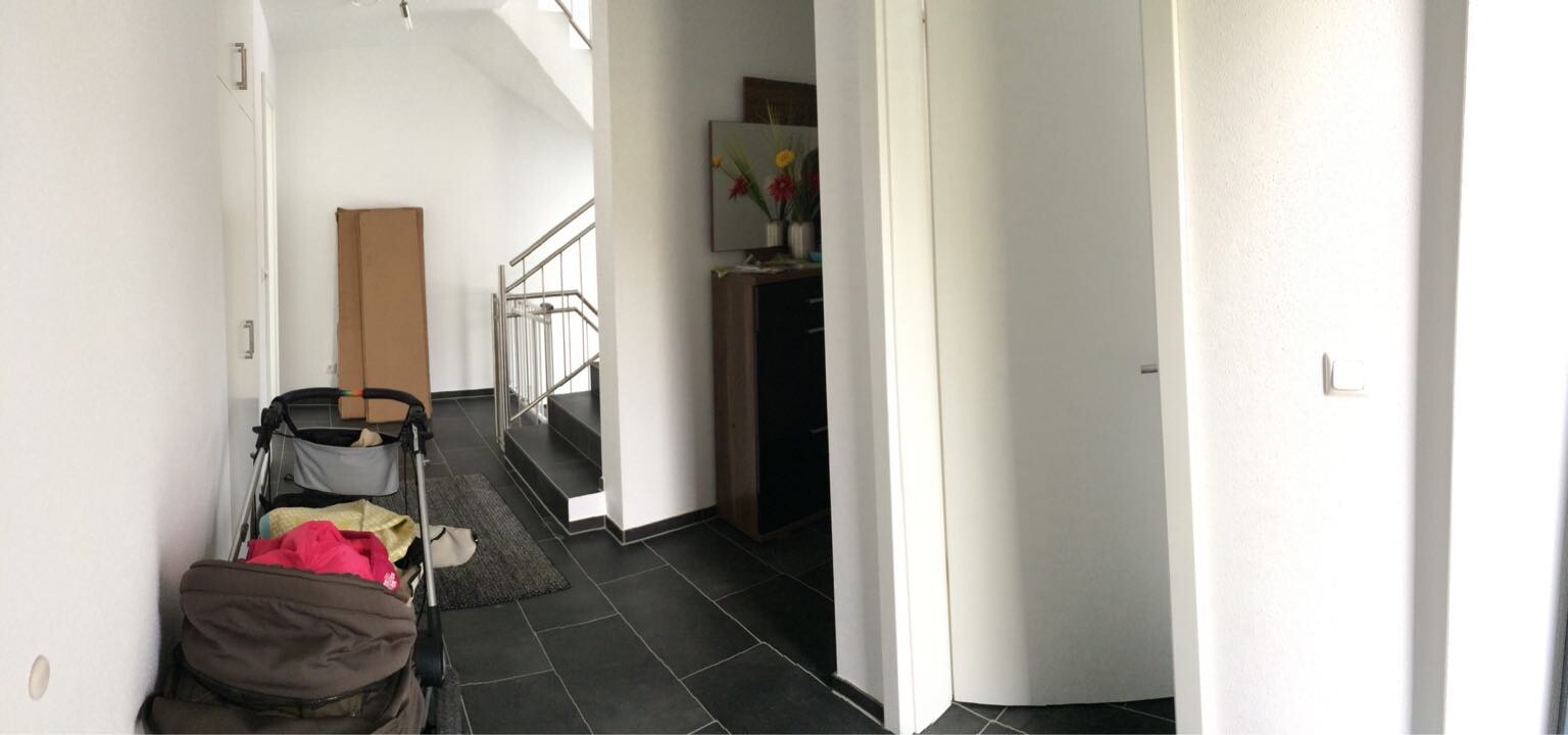Heller Flur mit dunklen Fliesen; linker Kinderwagen mit Kleidung, Treppe dahinter.