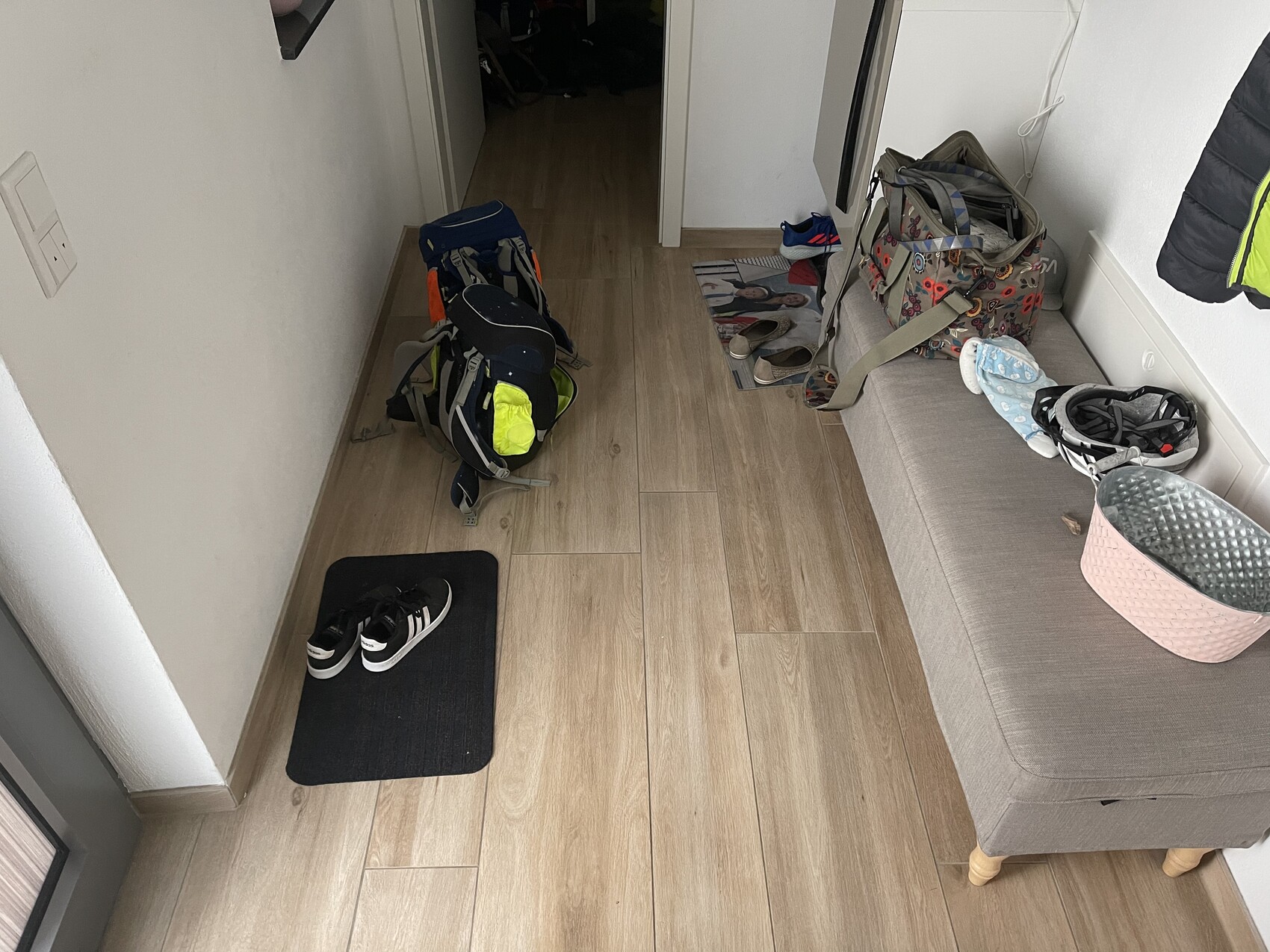 Flur mit gepacktem Rucksack, Schuhen auf Matte, Taschen und Gegenständen auf einer Couch, Holzboden.