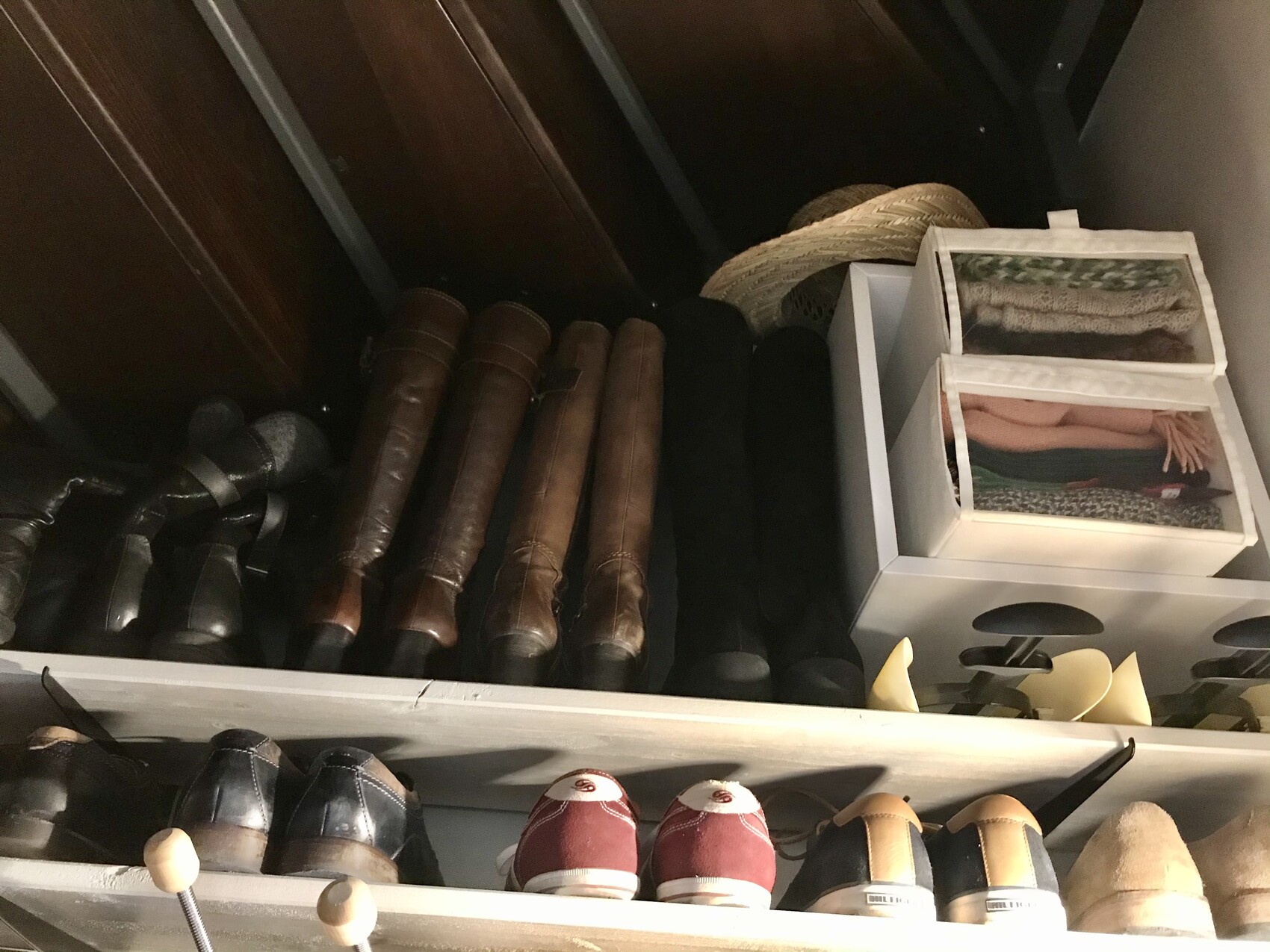 Schuhregal mit braunen Stiefeln und schwarzen Schuhen; Box mit Schals und Strohhut.