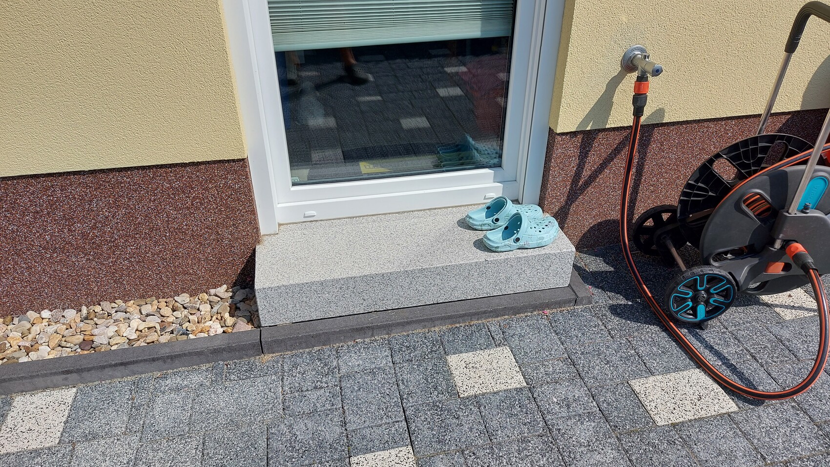 Eingangsbereich: graue Stufe vor Tür, blaue Crocs, Druckreiniger mit Schlauch daneben.
