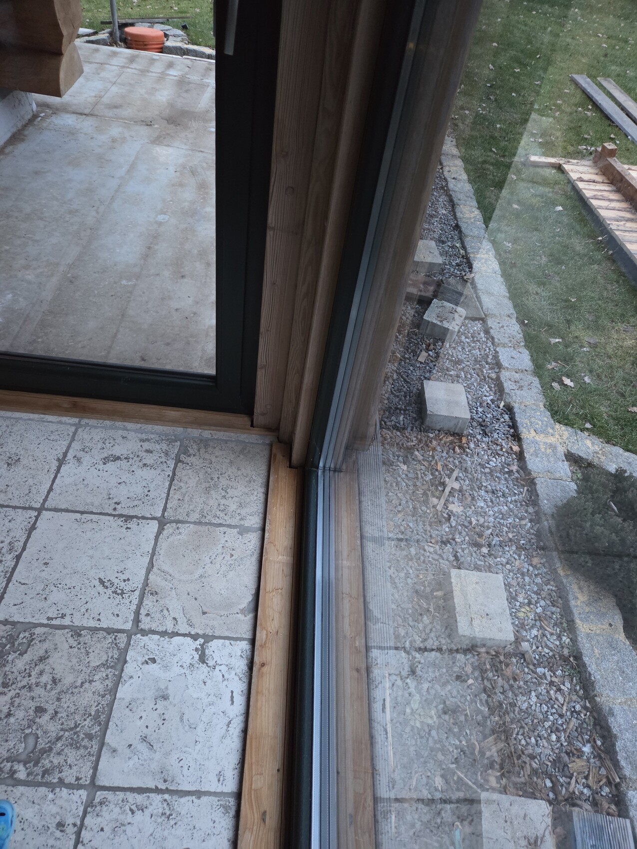 Blick durch glaeserne Terrassentuer auf unfertige Außenfläche mit Kies und Baumaterialien