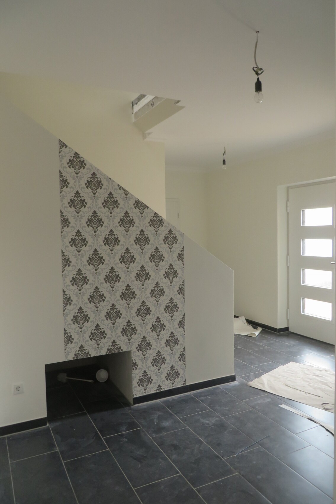 Foto eines renovierten Eingangsbereichs mit Treppe, gemusterter Wandverkleidung und dunklen Fliesen.