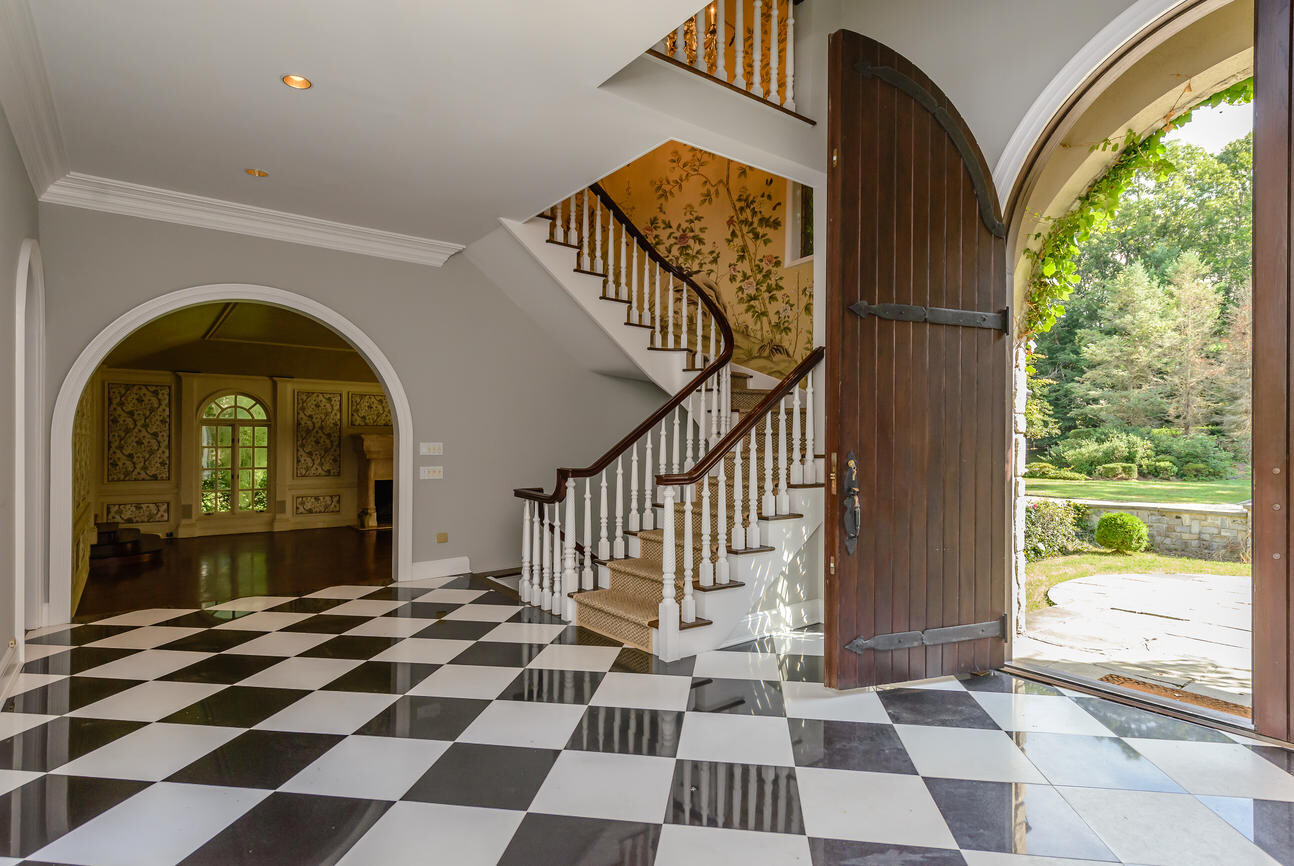 Großer Eingangsbereich mit Treppe, Schachbrettboden und offener Holztür zum Garten