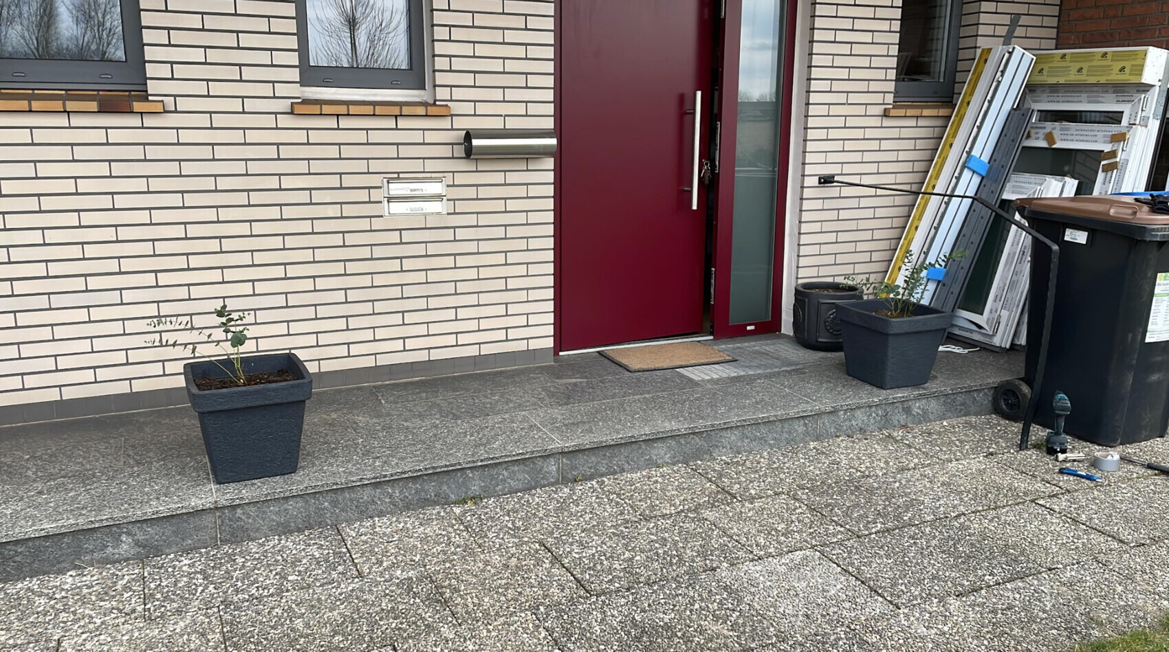 Frontansicht eines Hauses mit roter Tür, Treppenstufen und Pflanzkübeln am Eingangsbereich.