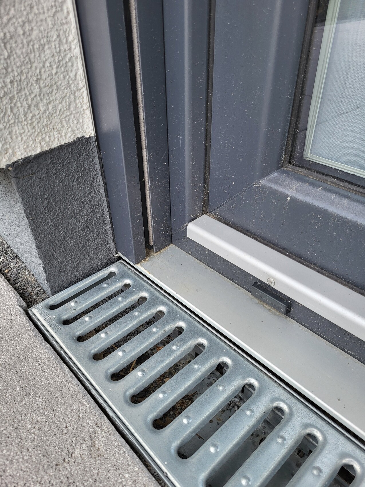 Dunkler Türrahmen mit Türschwelle; davor ein langes Metallgitter als Bodenablauf vor dem Eingang.