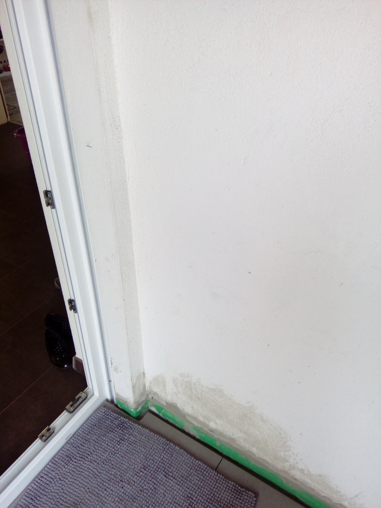 Eingangsbereich mit weißer Wand, Türrahmen und dunklem Bodenbelag; Tür offen