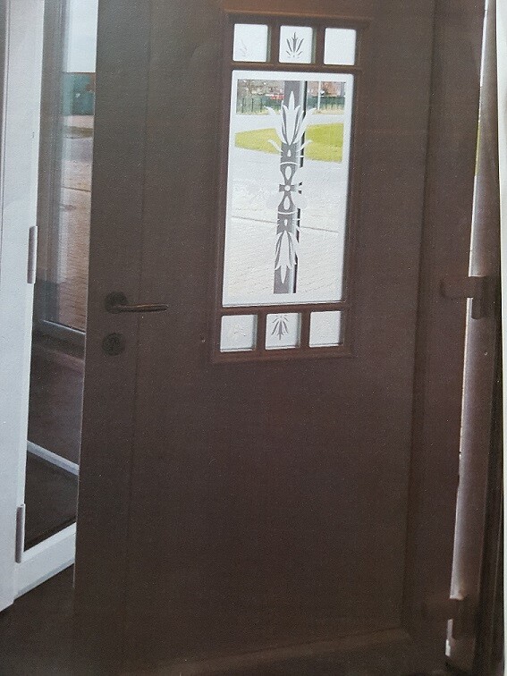 Dunkle Holztür mit dekorativem Glasfenster und vertikalem Pflanzenmuster.