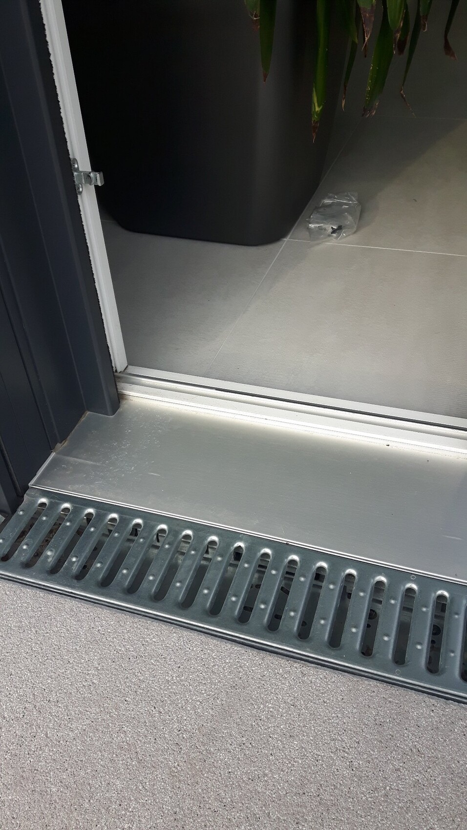 Offene Tür zum Innenraum; Metall-Schwelle, Gitterrinne vor dem Eingang, Plastikbeutel auf dem Boden.