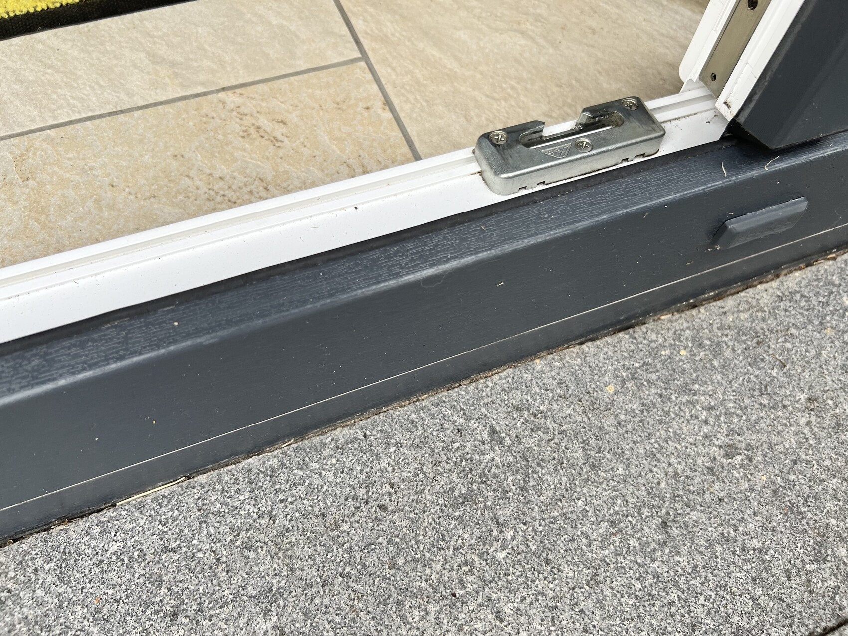 Offene Tür mit grauer Türschwelle und Metallriegel; innen beige Fliesen, außen Betonboden.