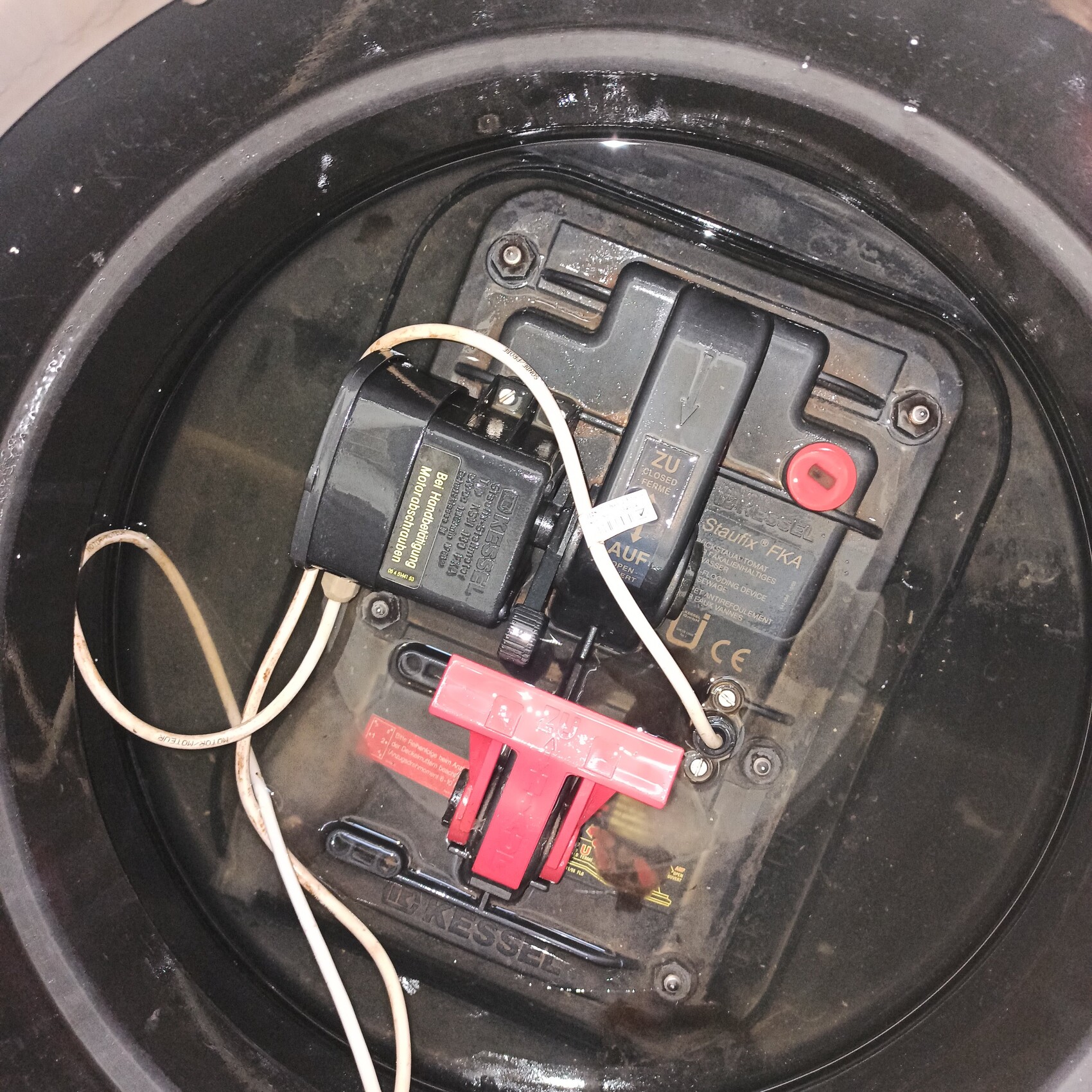Innenseite eines runden Gehäuses mit Batterieeinheit, Kabeln und rotem Sicherungsclip.