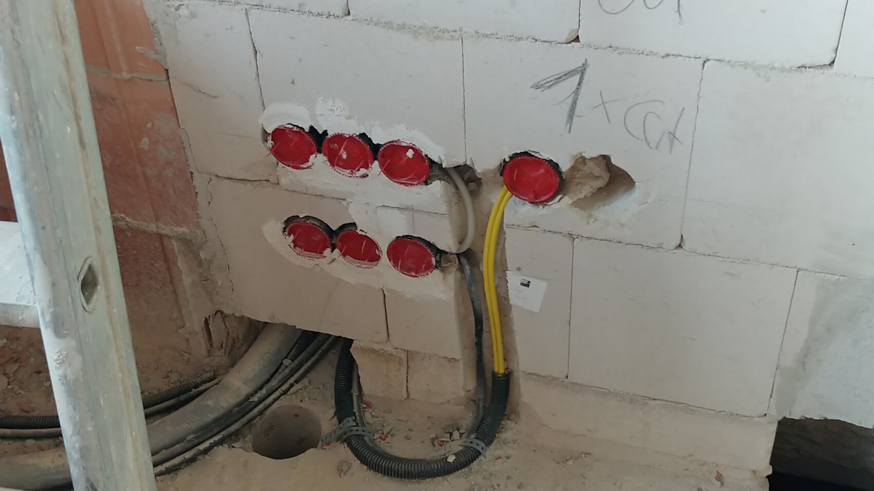Rohbauwand mit mehreren roten elektrischen Dosen und sichtbaren Kabeln für Strominstallation