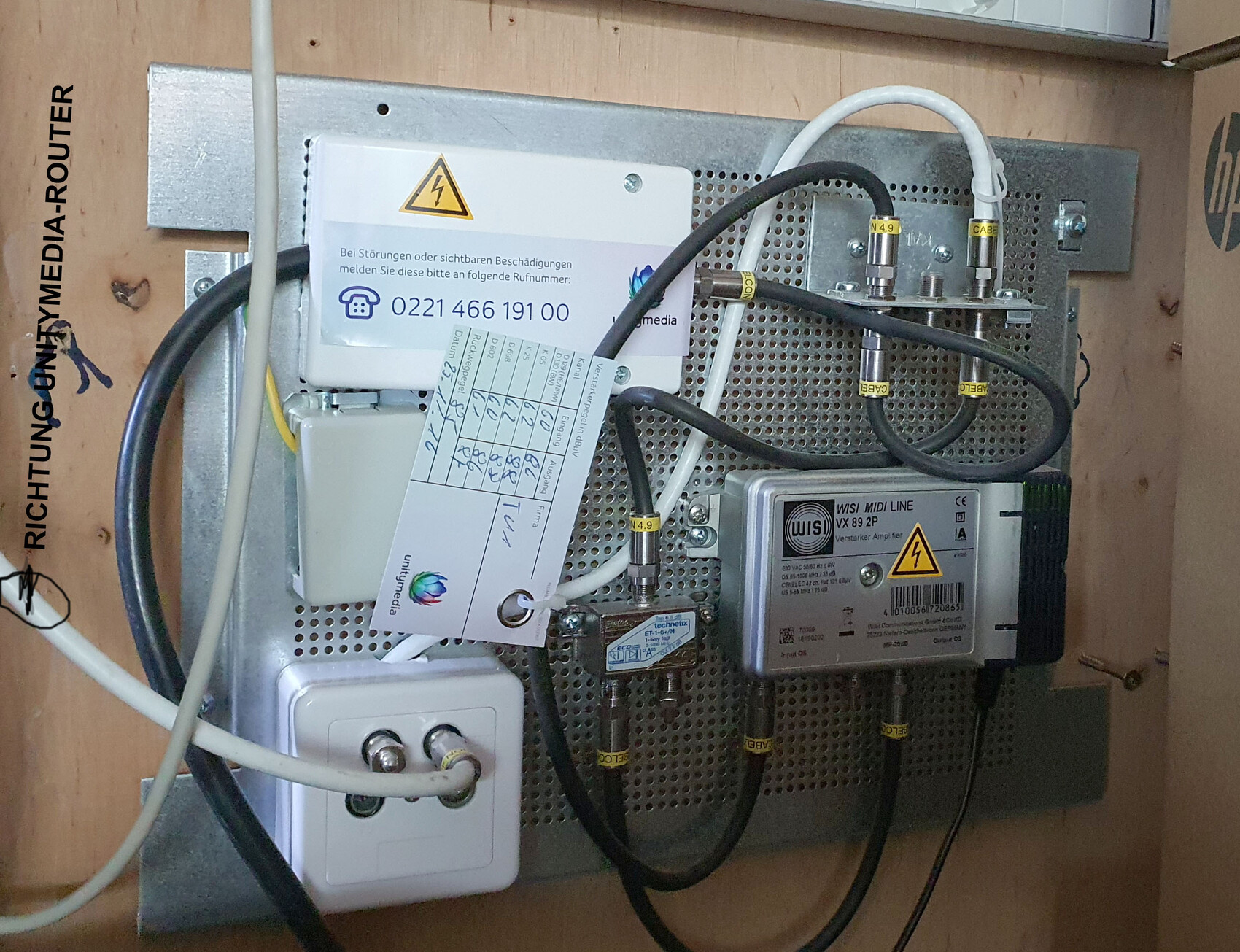 Elektronische Anlage mit Verstärker, Netzteil, Kabeln und Warnschild auf Metallplatte.