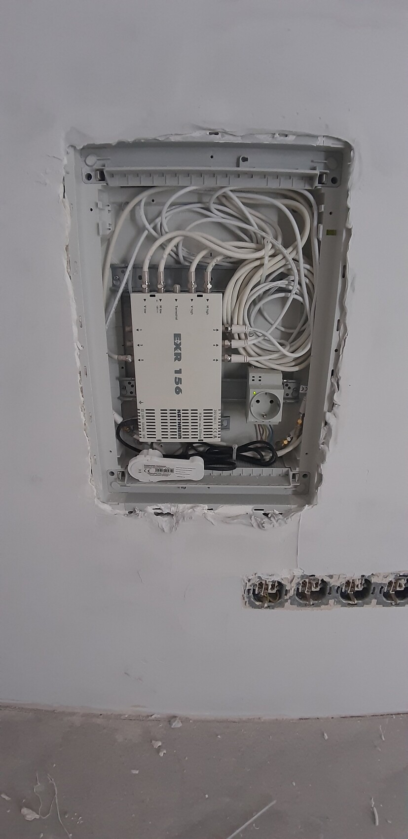 Verteilerschrank an der Wand mit vielen weißen Kabeln und Netzteil.