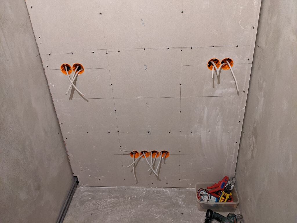 Gipskartonwand mit drei orangefarbenen Kabeldosen; weiße Kabel ragen heraus, Werkzeugkasten.