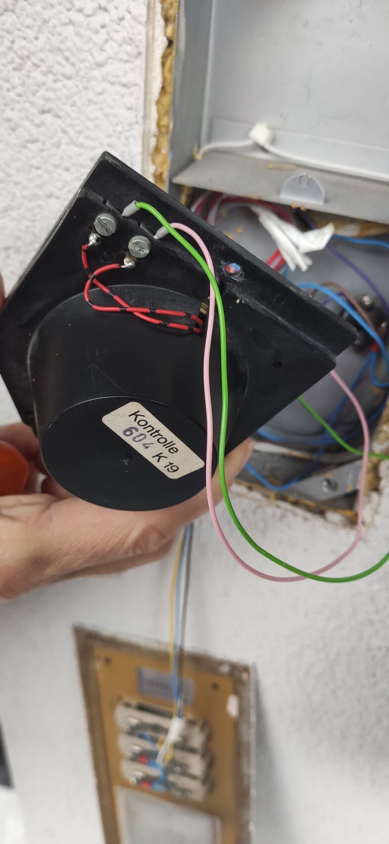 Hände halten schwarze Elektronikbox mit roten, grünen und rosa Kabeln; Aufschrift Kontrolle sichtbar.