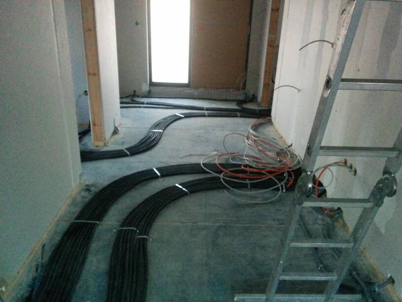 Innenraum einer Baustelle: schwarze Kabelbündel liegen in Bögen auf dem Boden; Leiter rechts.