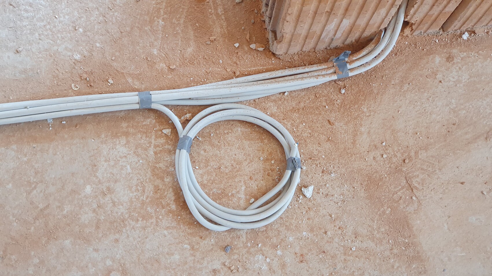 Weiße Elektrokabel liegen auf staubigem Baugrund, zu Schlaufen gebunden, eine Kabelecke sichtbar.