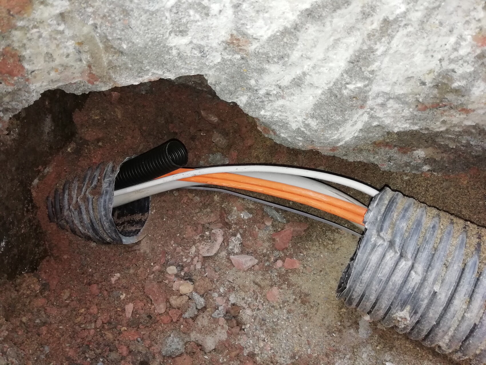 Offene elektrische Kabel im Wanddurchbruch eines Rohbaus mit orange- und weißen Leitungen.