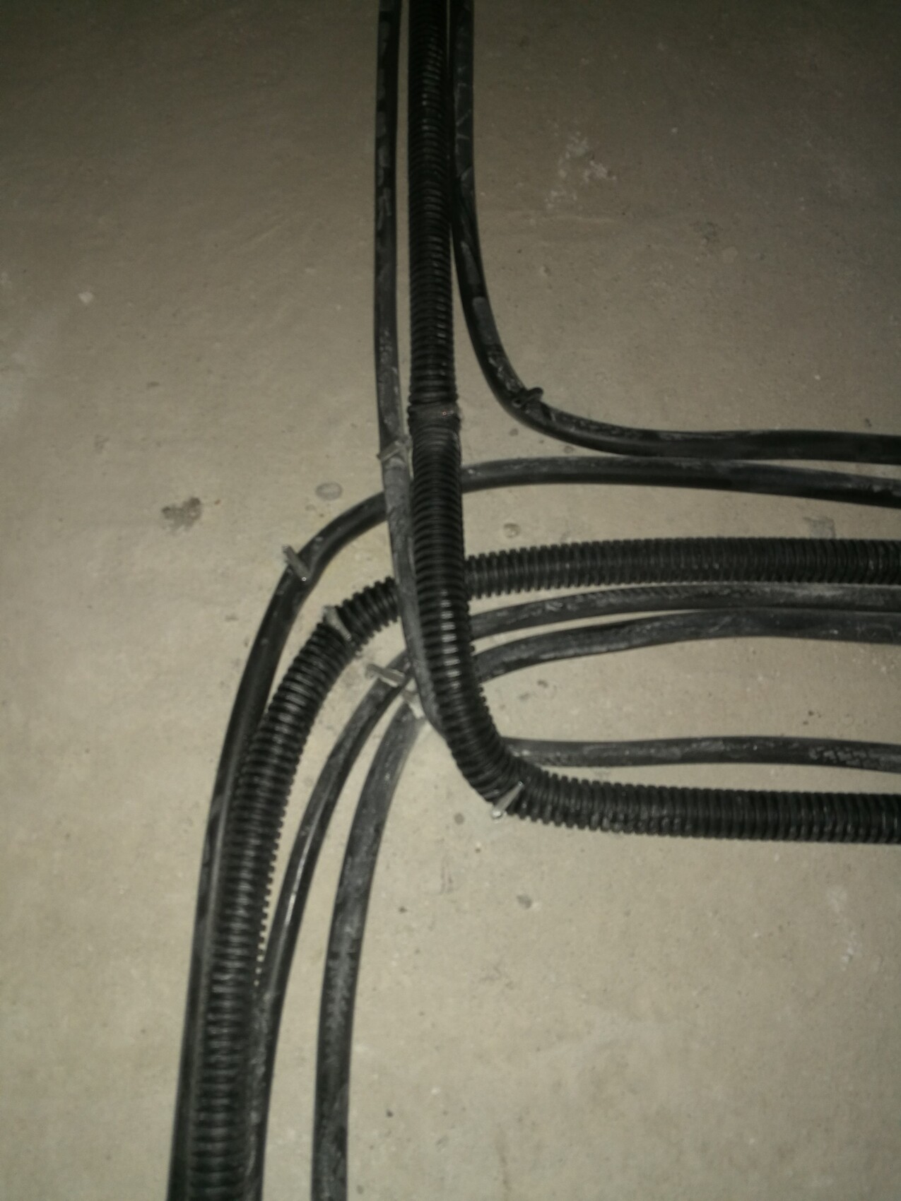 Kabelschläuche und Leitungen liegen auf rohem Betonboden einer Baustelle.