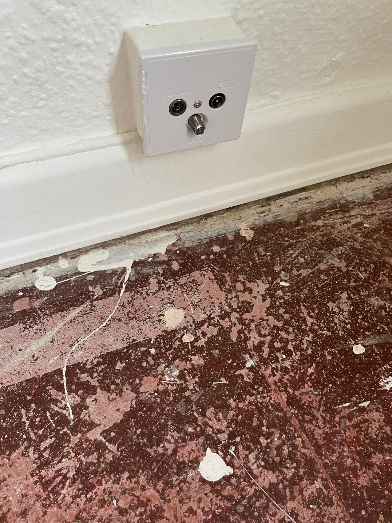 Wanddosenplatte mit L/R-Audioanschlüssen und Koaxialstecker; Boden mit Lackabplatzungen.