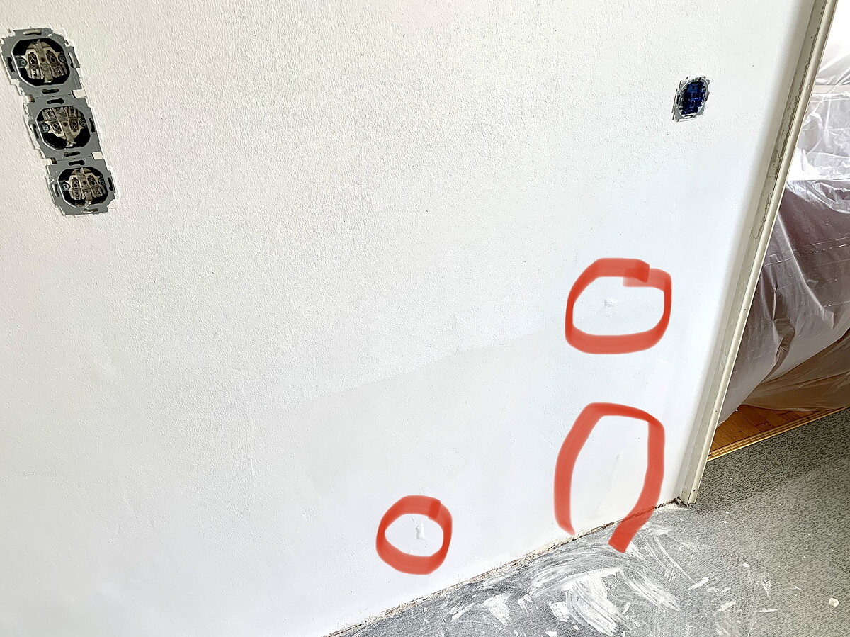 Weiße Wand mit offenen Elektro-Dosen links und drei roten Markierungen auf der Wand.