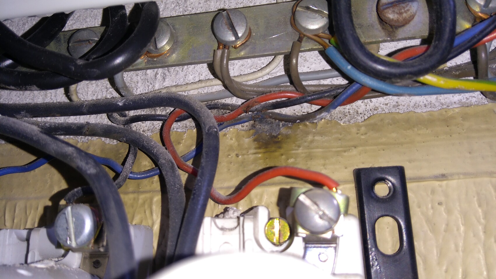 Verkabelung hinter einer Metallleiste mit Schrauben, Staub und farbigen Kabeln.