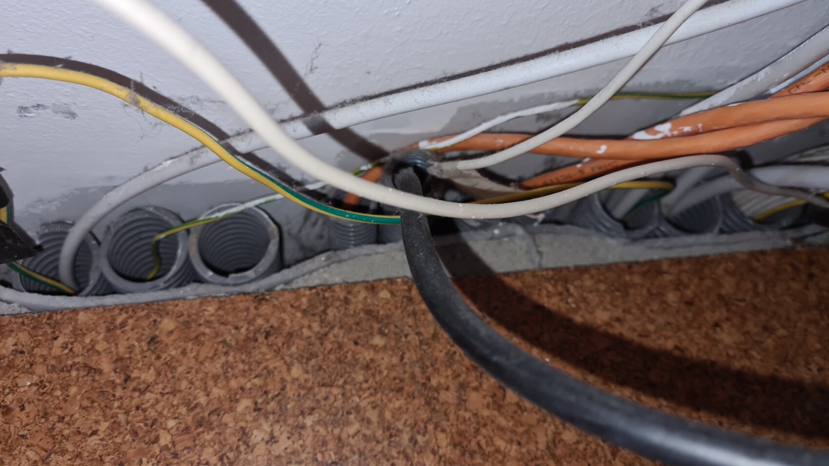 Kabelsalat hinter Wand mit mehreren Drahtkabeln (gelb/grün, orange, weiß) und Rohrdurchführungen.