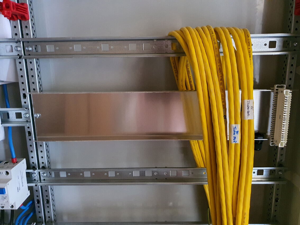 Gelbes Netzwerkkabelbündel hängt an einem Metallrack im Serverschrank; blaue Kabel daneben.
